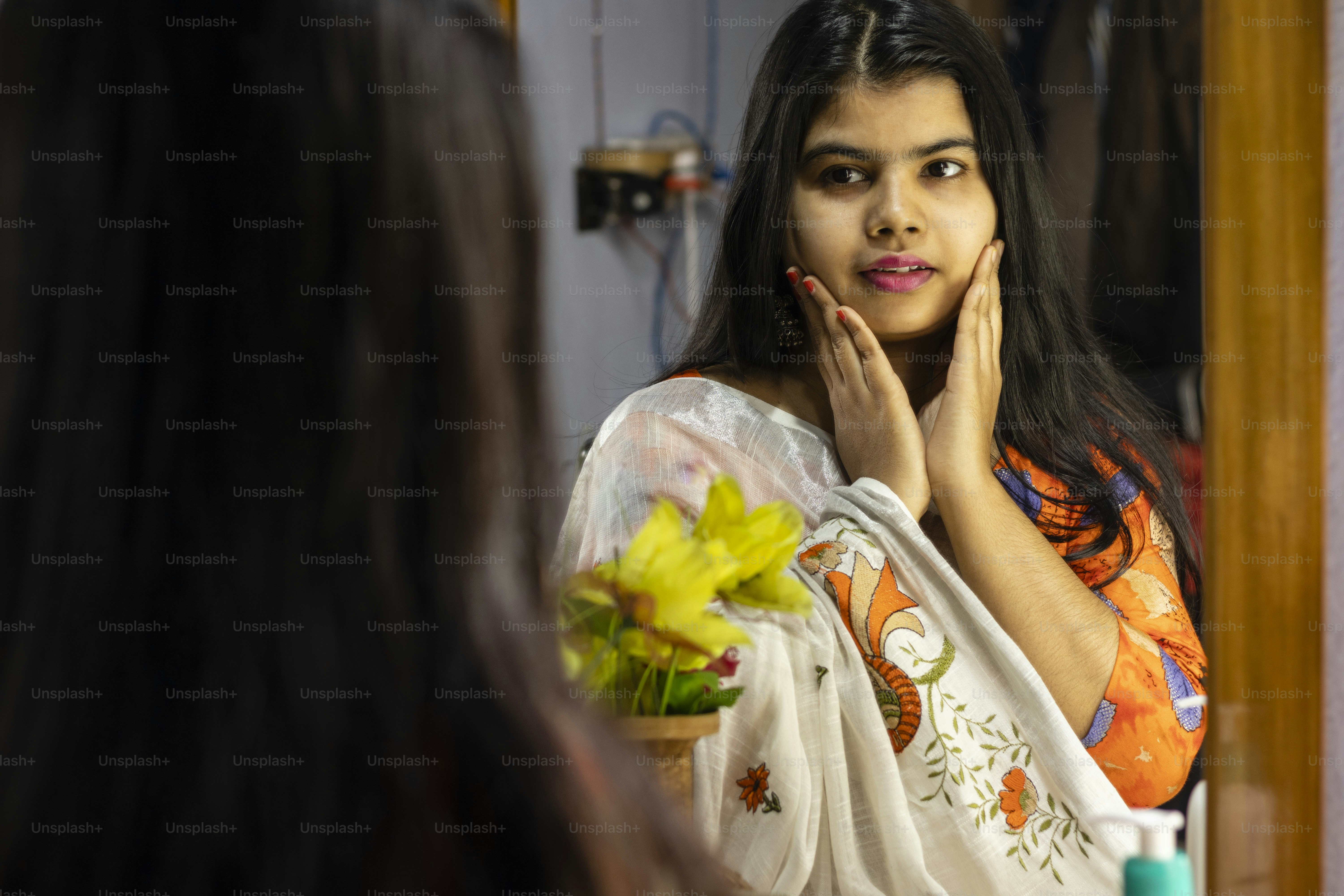 eine schöne indische Frau in weißem Saree, die sich mit lächelndem Gesicht im Spiegel betrachtet