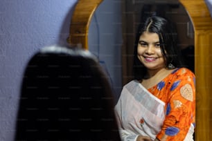 eine schöne indische Frau in weißem Saree, die mit lächelndem Gesicht vor dem Spiegel posiert