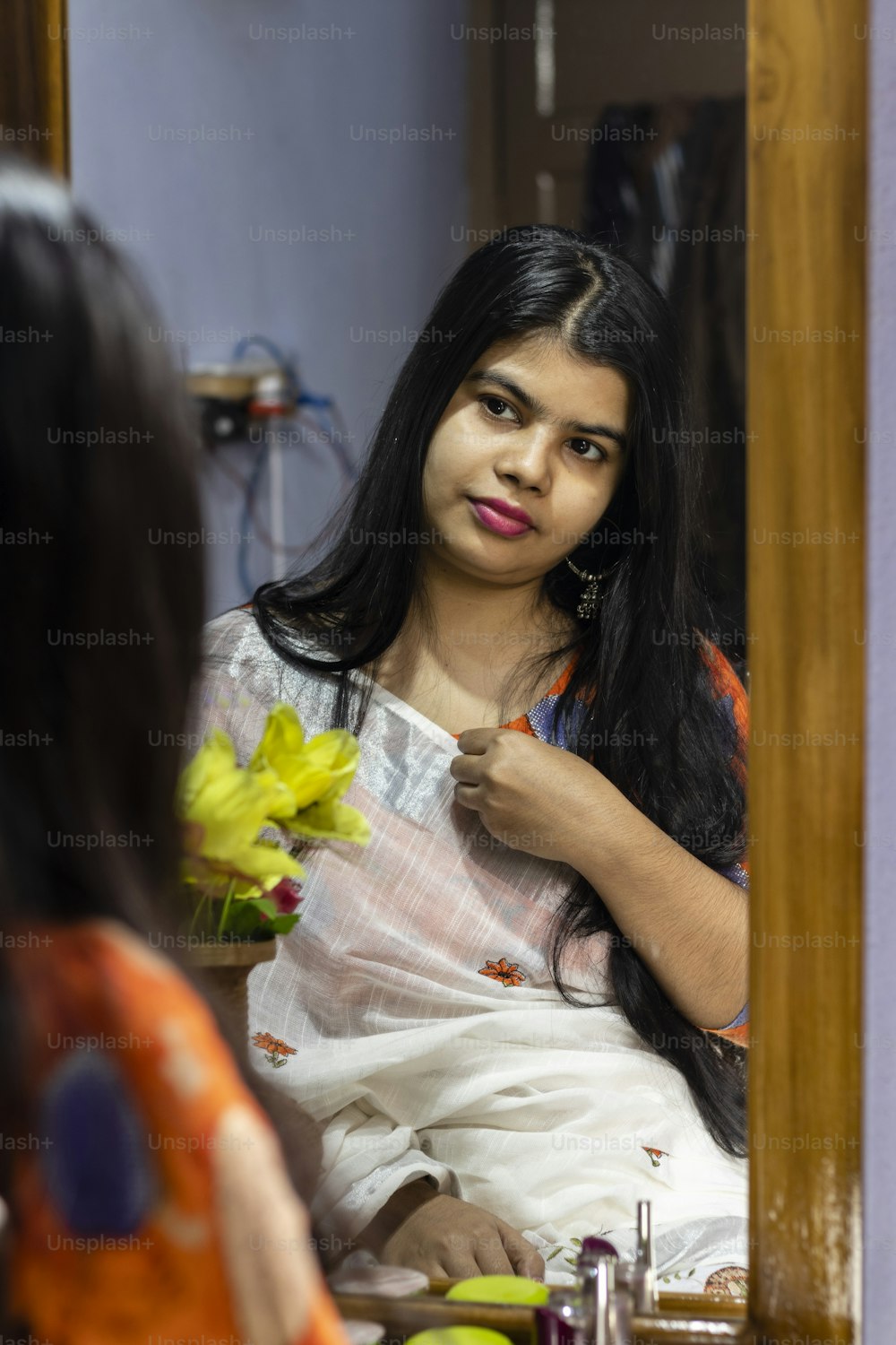 하얀 사리를 입은 아름다운 인도 여성이 웃는 얼굴로 거울에 비친 자신을 바라보고 있다
