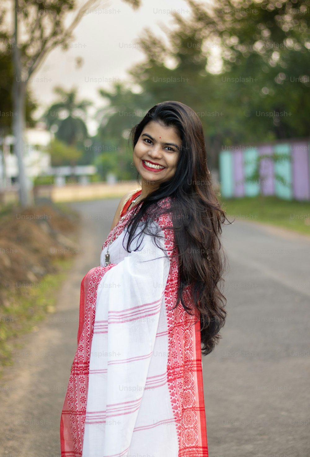 Una bella mujer india con sari rojo y cabello largo posando para la cámara en la carretera