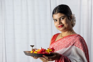 Une belle femme indienne en sari rouge tenant puja thali ou assiette de prière sur fond blanc