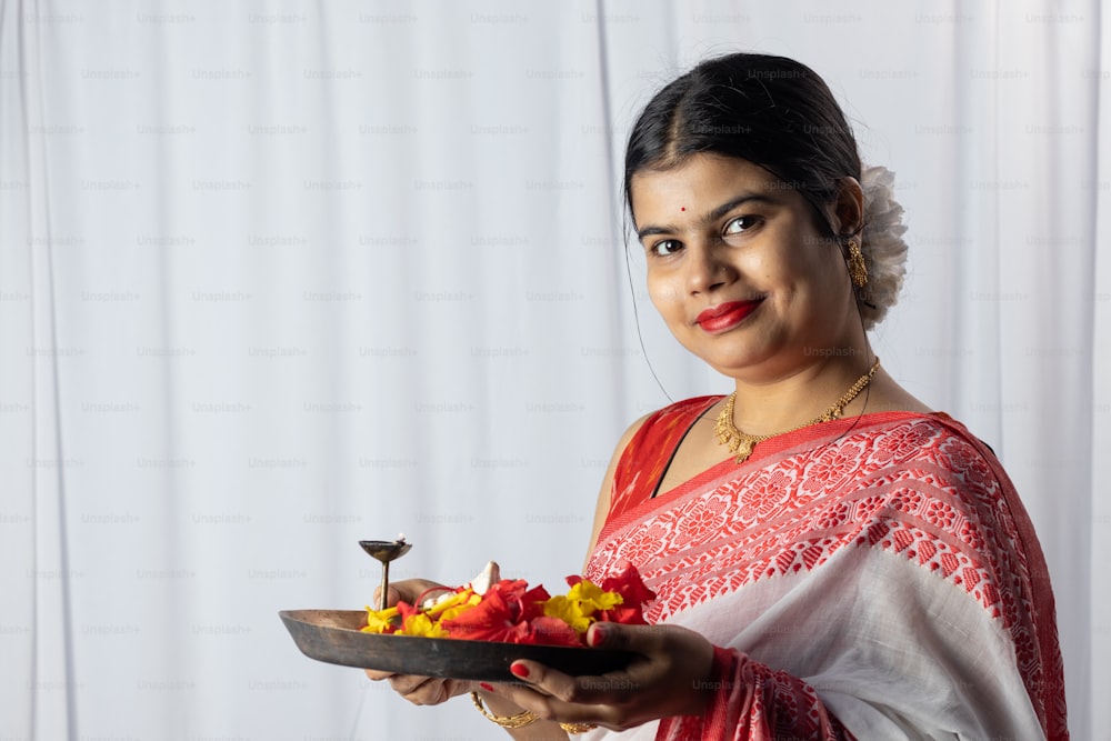 Una bella donna indiana in sari rosso che tiene puja thali o piatto di preghiera su priorità bassa bianca