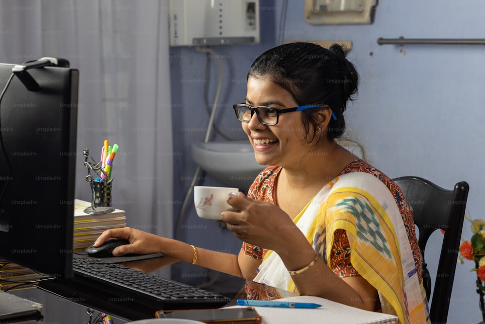 Mujer india en sari trabajando en computadora y tomando té en casa, concepto de trabajo desde casa