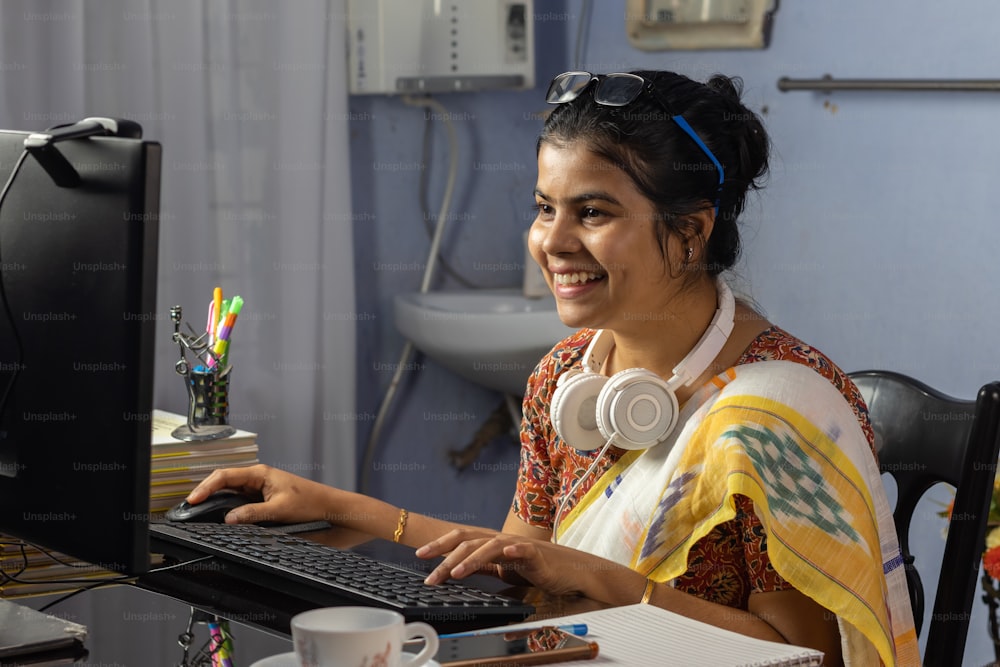 Indian woman in saree working on computer and talking over internet from home, online teaching concept
