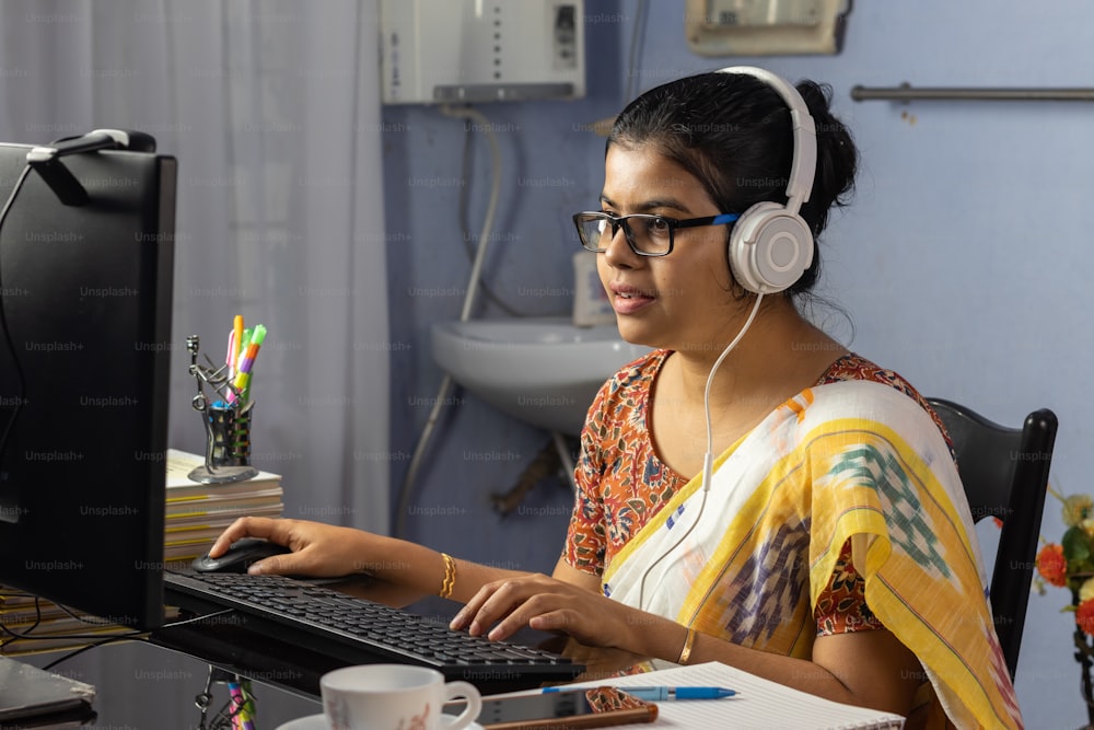 Indian woman in saree working on computer and talking over internet from home, online teaching concept