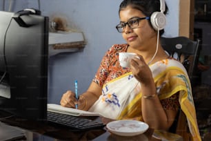 Indian woman in saree working on computer and taking tea at home, work from home concept