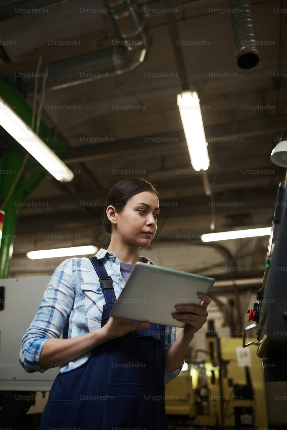 Young woman in overalls using digital tablet while working in the plant