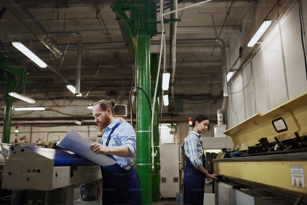 작업복을 입은 두 명의 육체 노동자가 인쇄 공장에서 선반 작업으로 바쁘다