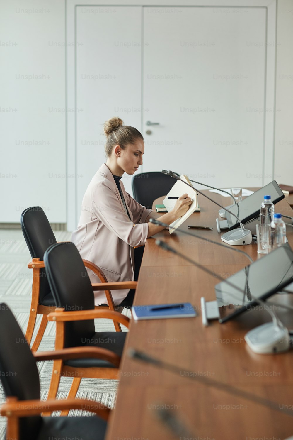 Young businesswoman sitting at conference table and writing plans and new ideas in her note pad before meeting at office