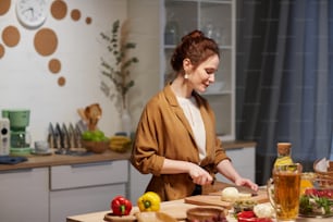 Mujer joven cortando queso en tabla de cortar en la mesa que cocina en la cocina doméstica