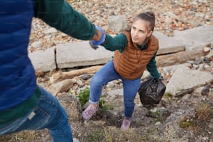 Man helping young woman up while they picking up garbage outdoors