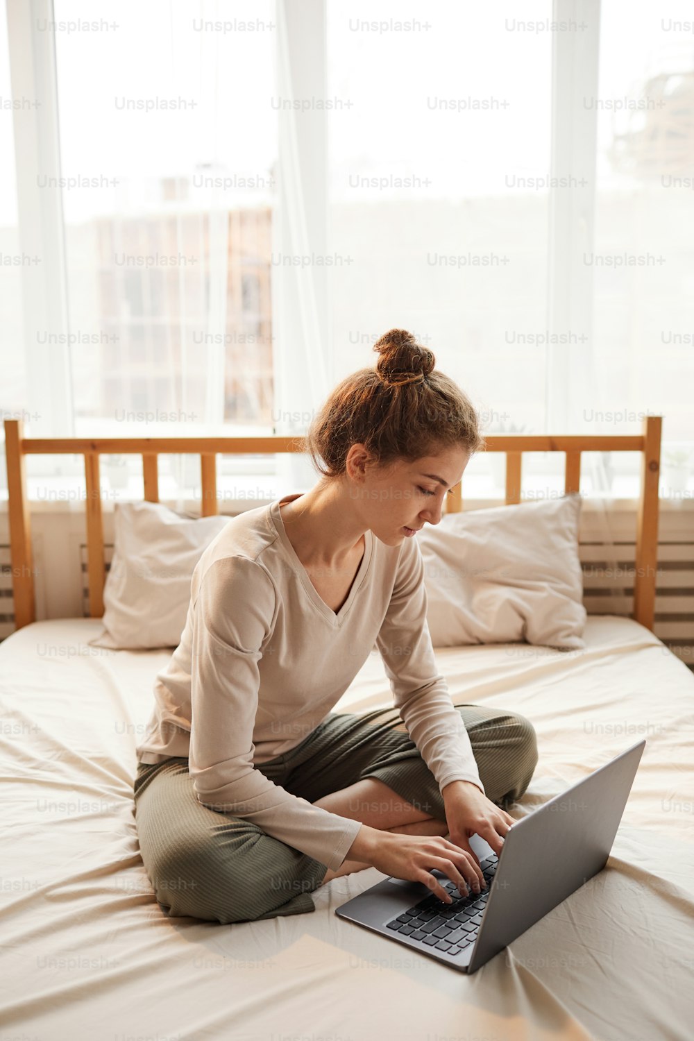 Young woman sitting on bed and typing on laptop she working online in the bedroom at home