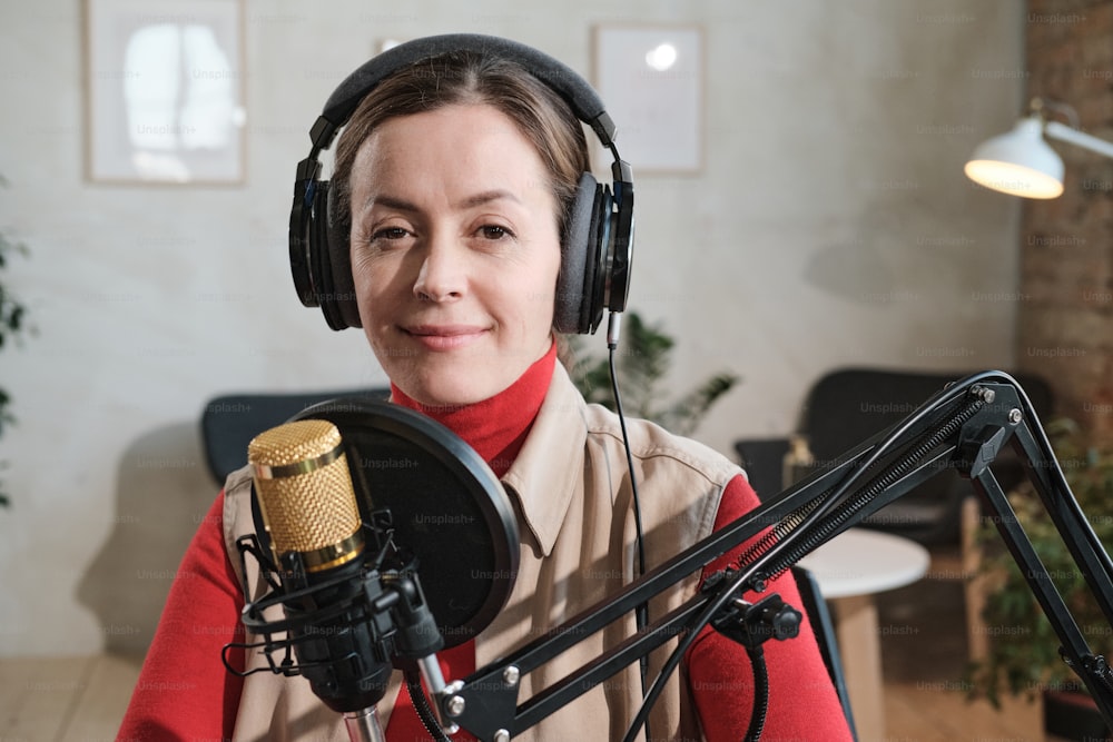 Portrait of young woman in headphones speaking in microphone during broadcasting she working at radio
