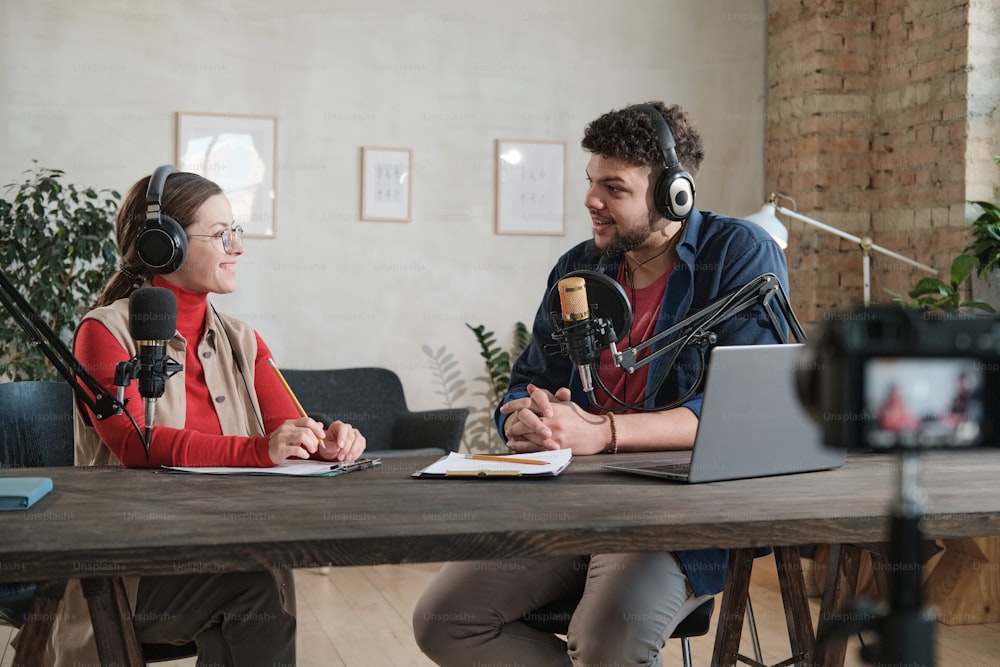 Giovane uomo in cuffia che intervista una donna al tavolo durante la trasmissione allo studio radiofonico