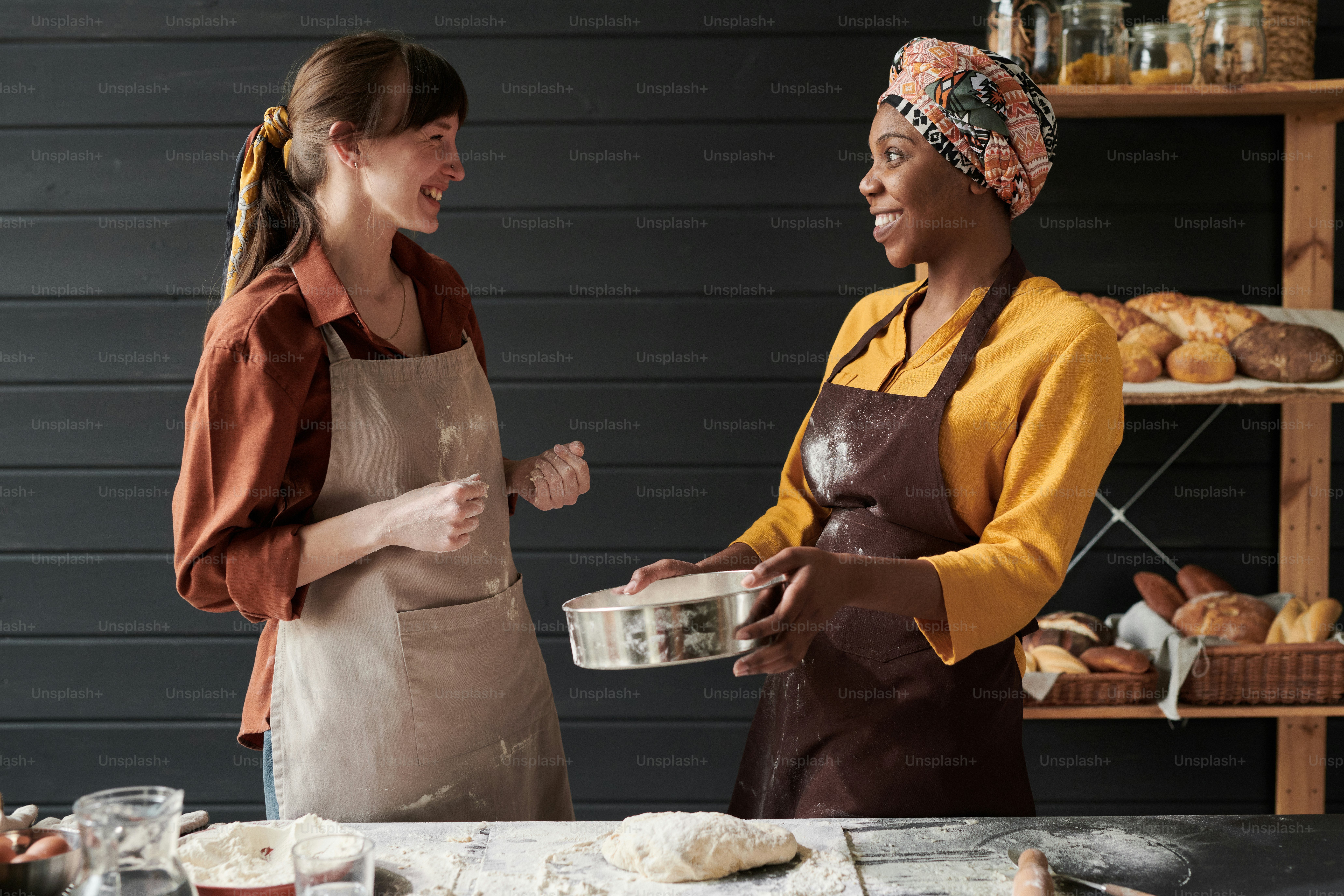 Two young bakers in aprons baking the bread together while standing in ...