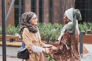 Two muslim women holding hands and smiling to each other during their meeting in the city