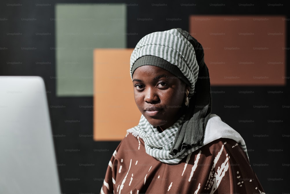 Close-up da jovem empresária da África em hijab olhando para a câmera enquanto sentada no escritório