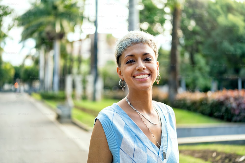 Portrait of fashionable millenial short haired woman with silver jewelry, earrings and necklace, smiling and looking to the camera. Beautiful girl walking on sunny summer day. Real people emotions. Lifestyle.