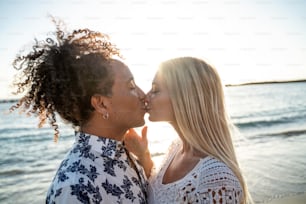 Multiethnic couple kissing, having fun together, dating on the beach during sunset. People in love. Honeymoon. Real emotions. Happiness.