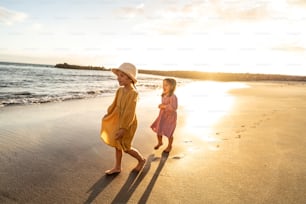 Bambini che giocano sulla spiaggia. Piccole sorelle che camminano in riva al mare al tramonto. Atmosfera per le vacanze estive in famiglia. Un sacco di spazio di copia.