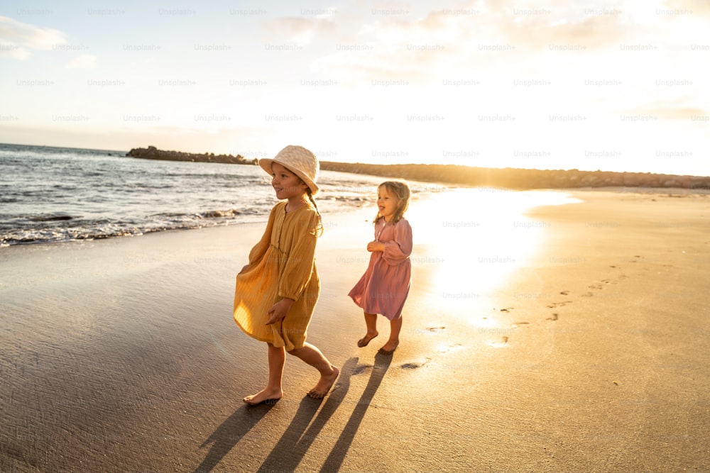 Crianças brincando na praia. Irmãzinhas andando na costa do mar ao pôr do sol. Vibrações de férias de verão em família. Muito espaço de cópia.