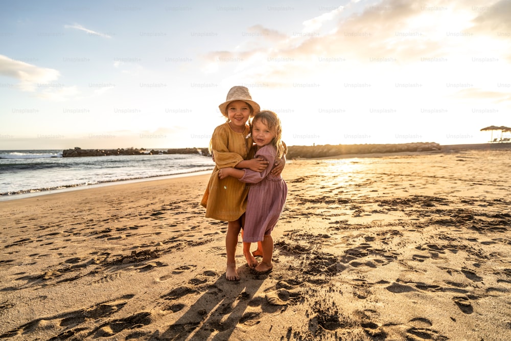 Bambini che giocano sulla spiaggia. Piccole sorelline che si divertono in riva al mare al tramonto. Atmosfera per le vacanze estive in famiglia. Un sacco di spazio di copia.