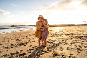 Bambini che giocano sulla spiaggia. Piccole sorelline che si divertono in riva al mare al tramonto. Atmosfera per le vacanze estive in famiglia. Un sacco di spazio di copia.