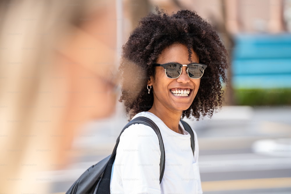 ファッショナブルなサングラスをかけ、屋外でポーズをとるアフロの髪型を持つ自然な笑顔の若い女性のポートレート。夏の雰囲気。