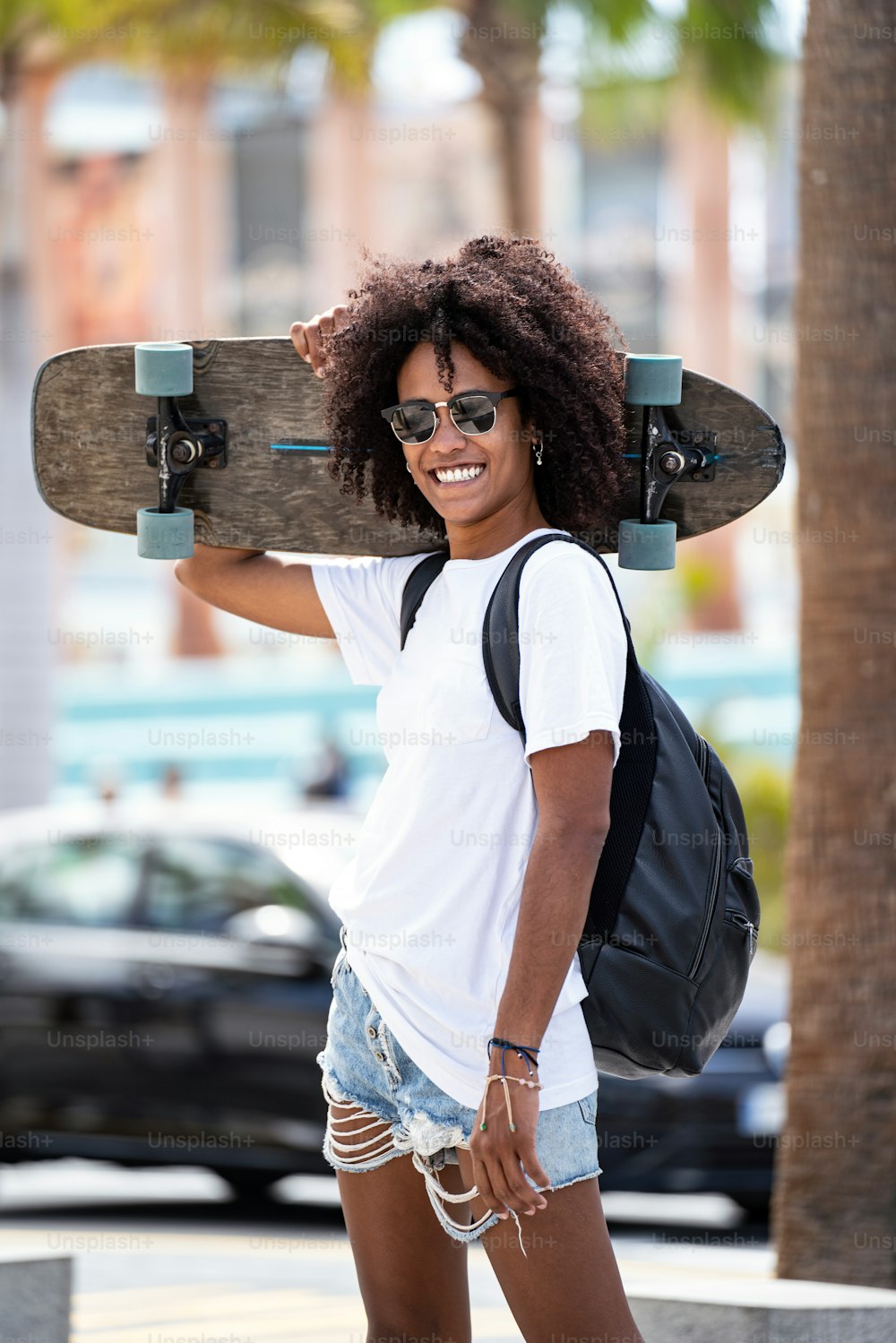 Young afro woman smiling and posing with skateboard. Sport female model in urban style. Street style outfit. Hipster girl skateboarding. Hobby.