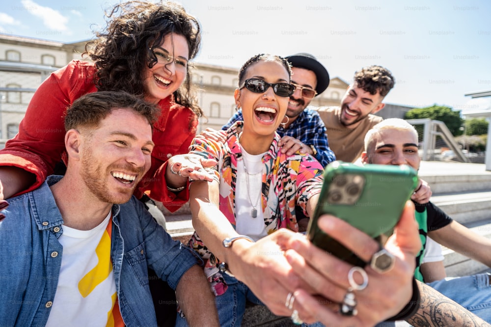 Group of happy multiracial students, friends using smartphone outdoors, watching social media and laughing, having fun together. Fashionable people making a selfie. Tourist. Travel.