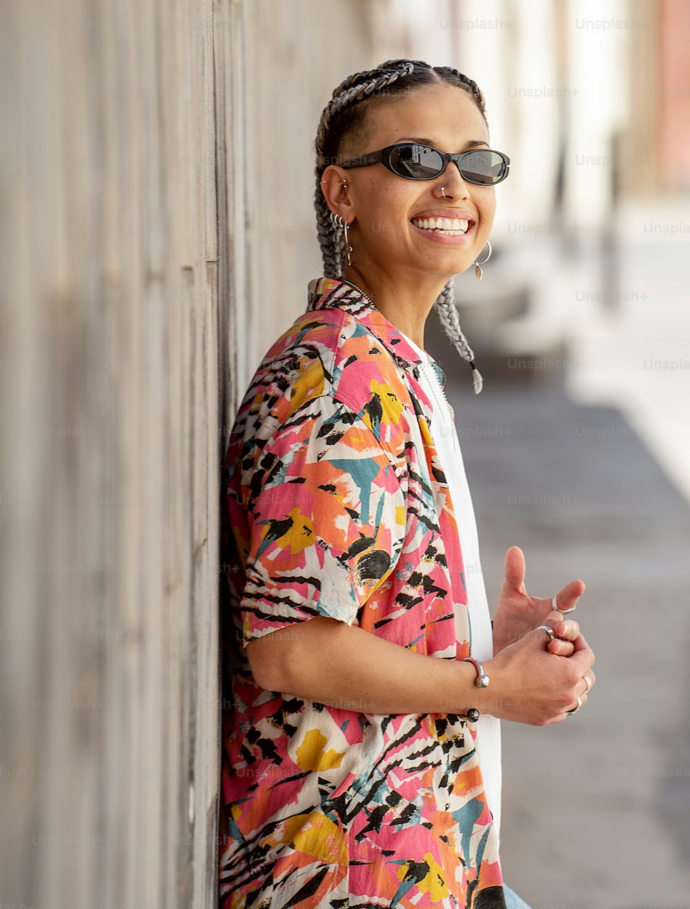 Happy smiling young hispanic woman posing on the city street . Girl wearing fashionable shirt, sunglasses and a lot of jewelry. Real people emotions. Lifestyle. Outdoor photo.