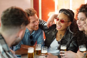 Amici che parlano e si divertono insieme al bar, bevendo birre. Gruppo multiculturale di studenti. Emozioni di persone reali. Stile di vita.