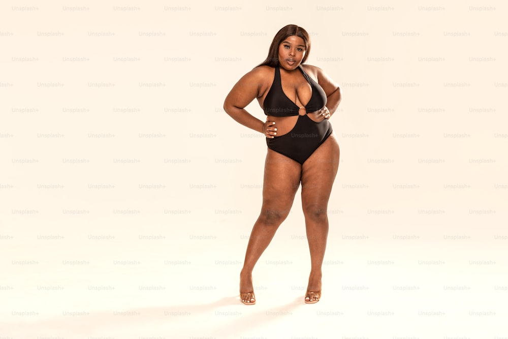 Full-length photo of beautiful plus size dark skinned woman posing on light  gray, wearing black fashionable swimsuit. Body positive, conscious concept.  photo – Bikini model Image on Unsplash