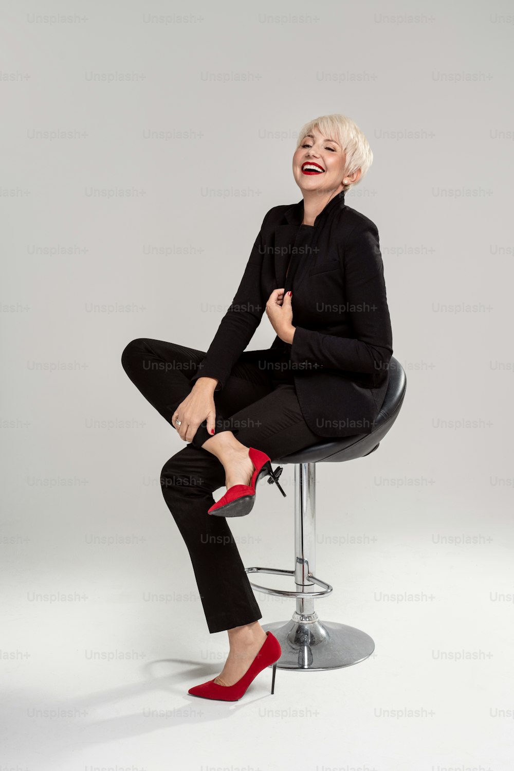 Successful businesswoman with short fashionable hairstyle and glamour makeup, looking at camera, laughing, sitting on the chair. Full length photo. Copy space. Success.