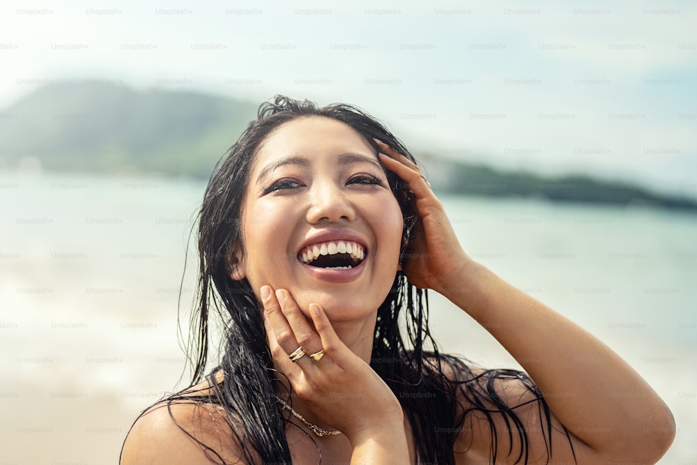 Porträt einer schönen jungen asiatischen Frau mit erstaunlichem zahnigem Lächeln. Mädchen mit nassen Haaren genießt sonnigen Tag am Strand. Fröhliches Urlaubs-Lifestyle-Konzept. Echte Menschen, Emotionen. Reisende.