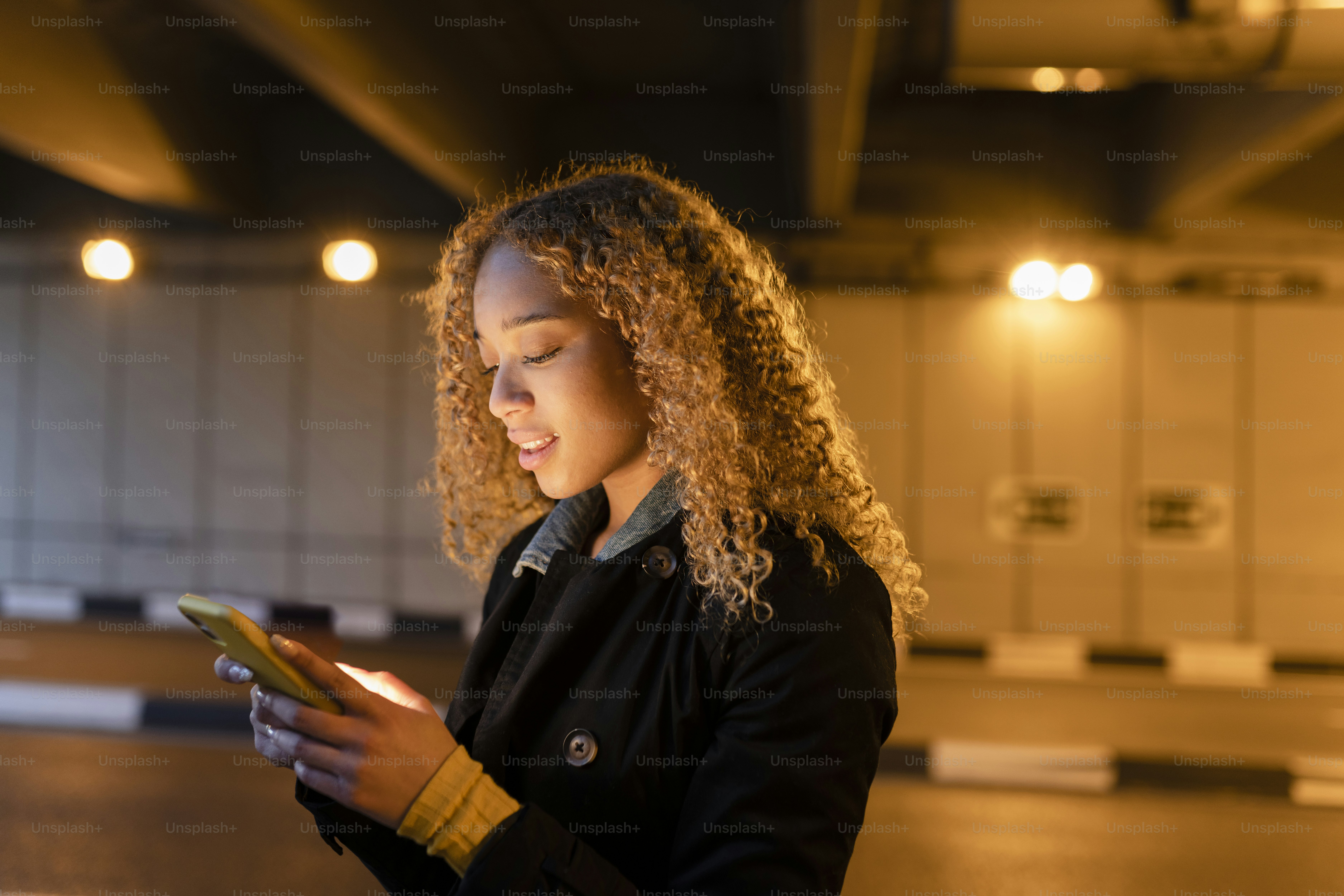 Bella donna con i capelli biondi ricci, di notte, in città, guardando il suo cellulare
