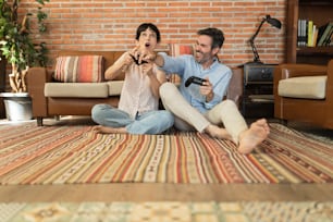 Mature couple having fun at home playing a video game with joysticks in hands. happy hispanics in apartment