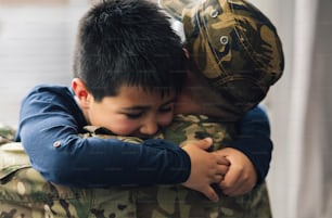 A military father and his son embrace in the living room of their home. The son smiles happily at the camera - concept hugging daddy -.