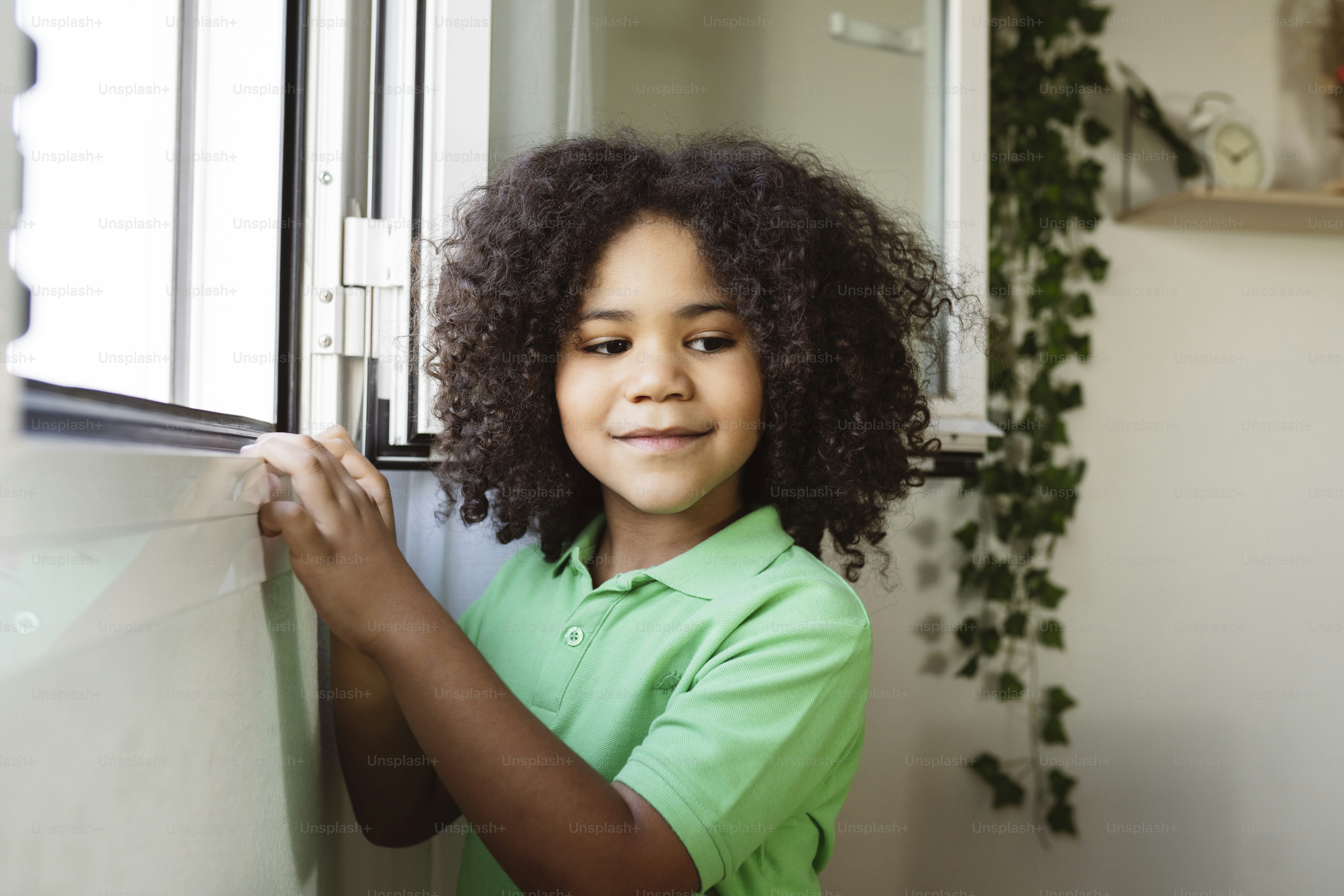 an afro american boy with afro hair in the window of his house