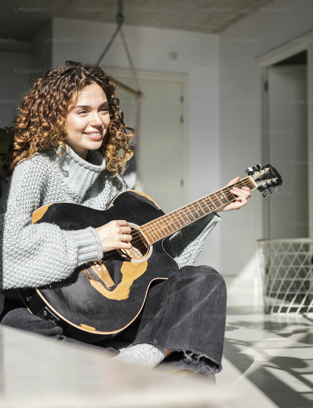 pretty hispanic curly hair woman playing guitar at home