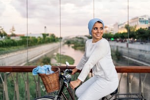 Cheerful muslim woman riding her bicycle next to her on the footbridge in a sunny day.