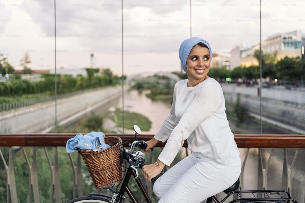 Cheerful muslim woman riding her bicycle next to her on the footbridge in a sunny day.