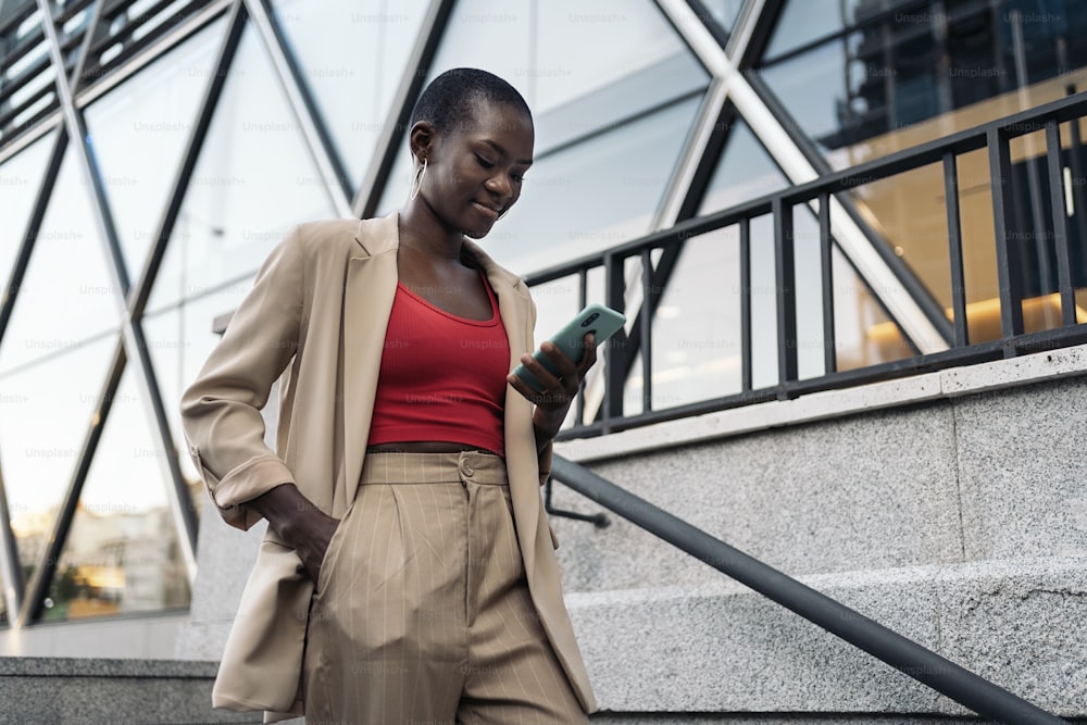 Vista lateral recortada de una mujer adulta joven afroamericana con cabello corto bajando escaleras usando el teléfono en la ciudad