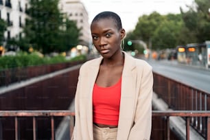 Porträt einer afroamerikanischen jungen Frau mit kurzen Haaren, die auf einer Fußgängerbrücke in der Stadt steht und in die Kamera schaut