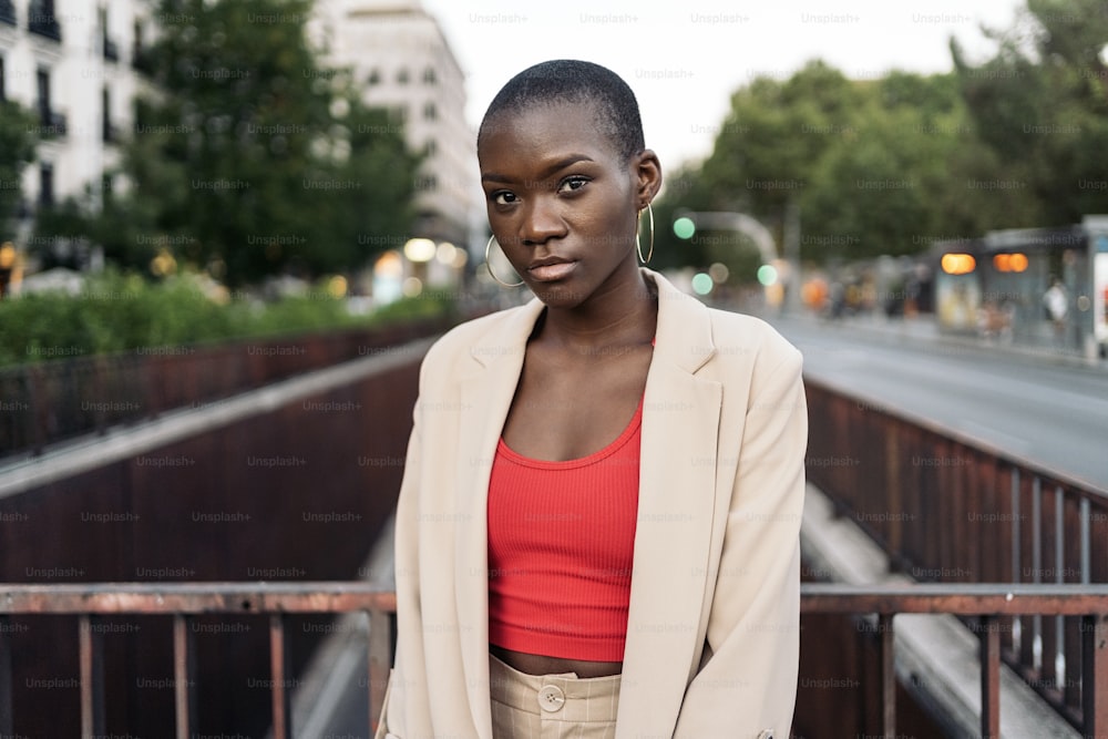 Ritratto di una giovane donna afroamericana con i capelli corti in piedi e guardando la macchina fotografica su una passerella in città