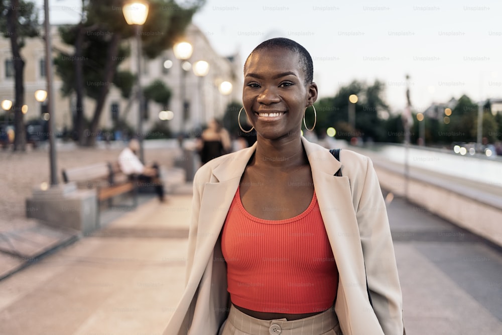 Vista frontale di una giovane donna adulta afroamericana alla moda che ride mentre cammina in città al tramonto