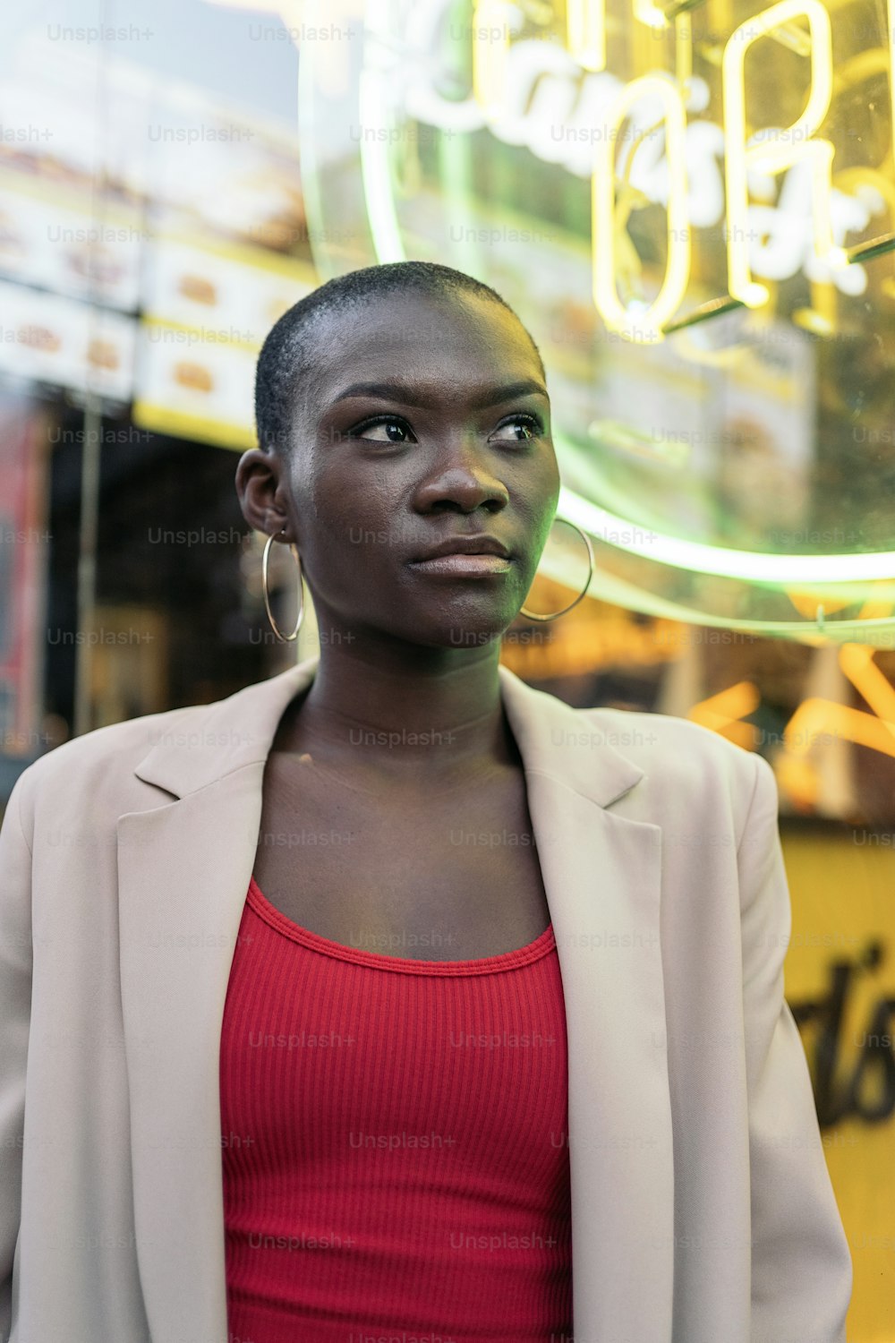 Portrait of a stylish african american adult woman standing and looking away with neon sign behind in the city