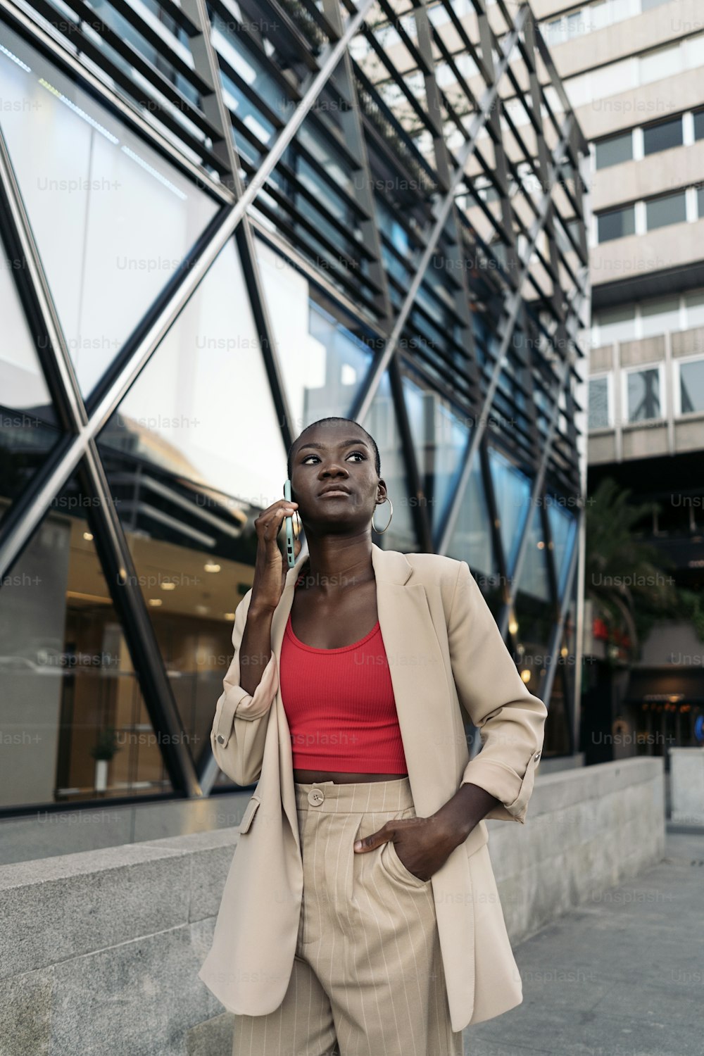 Elegante joven afroamericana con la mano en el bolsillo con el pelo corto caminando por la ciudad mirando hacia otro lado mientras habla con su teléfono.