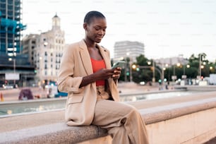 휴대전화를 사용하여 분수 가장자리에 앉아 있는 패셔너블��한 여성의 전체 길이 보기