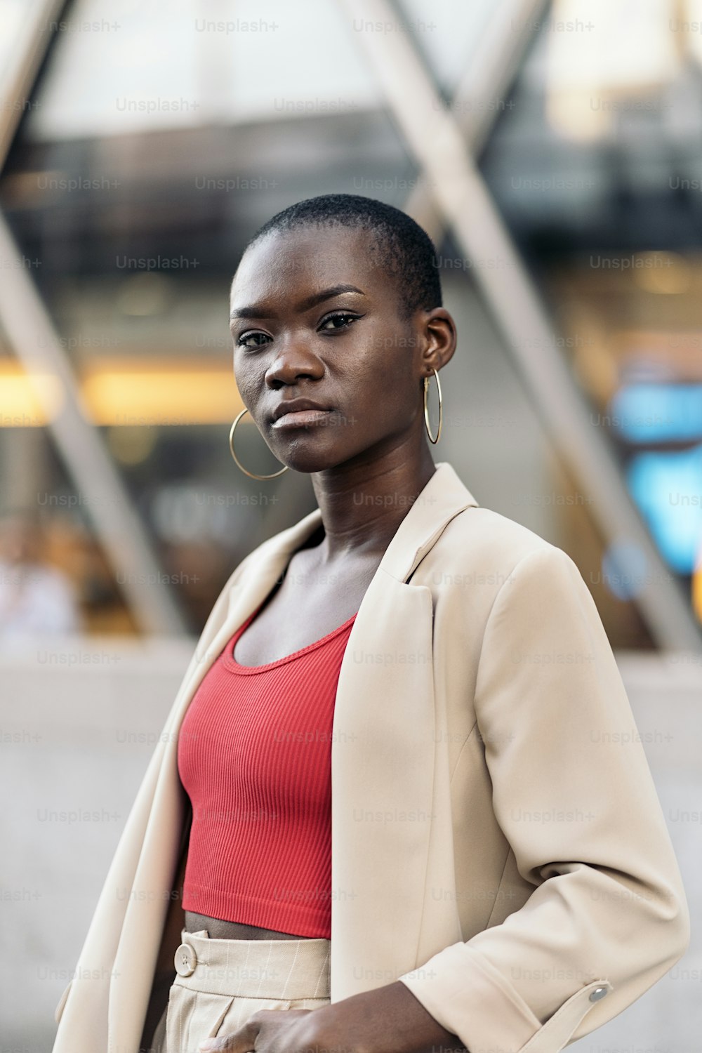 Vertikales Bild einer eleganten afroamerikanischen jungen erwachsenen Frau mit kurzen Haaren, die in der Stadt steht und in die Kamera schaut